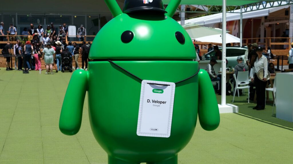 Googleのロゴと『D. Veloper』の名札を首から下げた緑のAndroidロボット像が屋外に立つ写真。Googleの開発テストで自社Geminiは合格率8%の7位だった