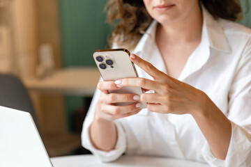 ノートパソコンの横で、白いシャツの女性がスマホを両手で持って操作している手元の写真