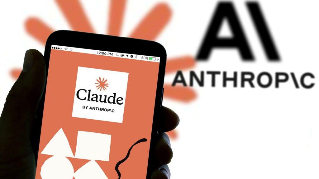 手元のスマートフォンにClaudeのロゴ画面が表示され、背景にANTHROPICのロゴと文字が見える写真。Anthropic、Claude Duet公開 日本は10月時点で使えない