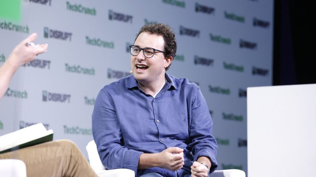 TechCrunch Disruptのロゴが並ぶ壁の前で、マイクを付けた眼鏡の男性が笑いながら話している写真。Claude Code、トーバルズ氏がカーネル改良に使う 問題は10件残る