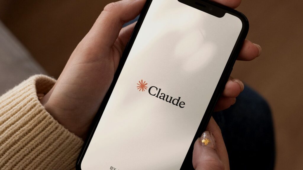 手元でClaudeのロゴが表示されたスマートフォンの画面を持つ人物の写真。Claude LSVP開始、創薬の制限が緩むのはTeamの2席からだ
