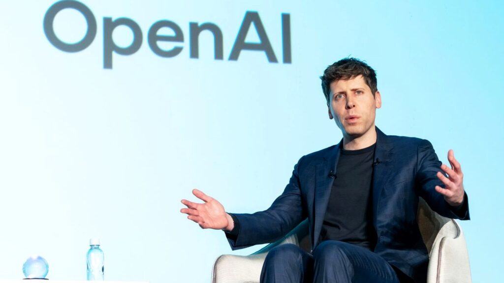 背景にOpenAIのロゴが映るステージで、スーツ姿の男性が両手を広げて話している写真。OpenAI、dotsをスマホ対応 月3,000円のPlusでは作れない