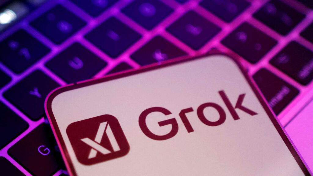 紫に光るノートパソコンのキーボードの上にGrokのロゴを表示したスマートフォンを置いた写真。SpaceXAI、Grok Voice 3.0は0.81秒 日本語は未公表だ