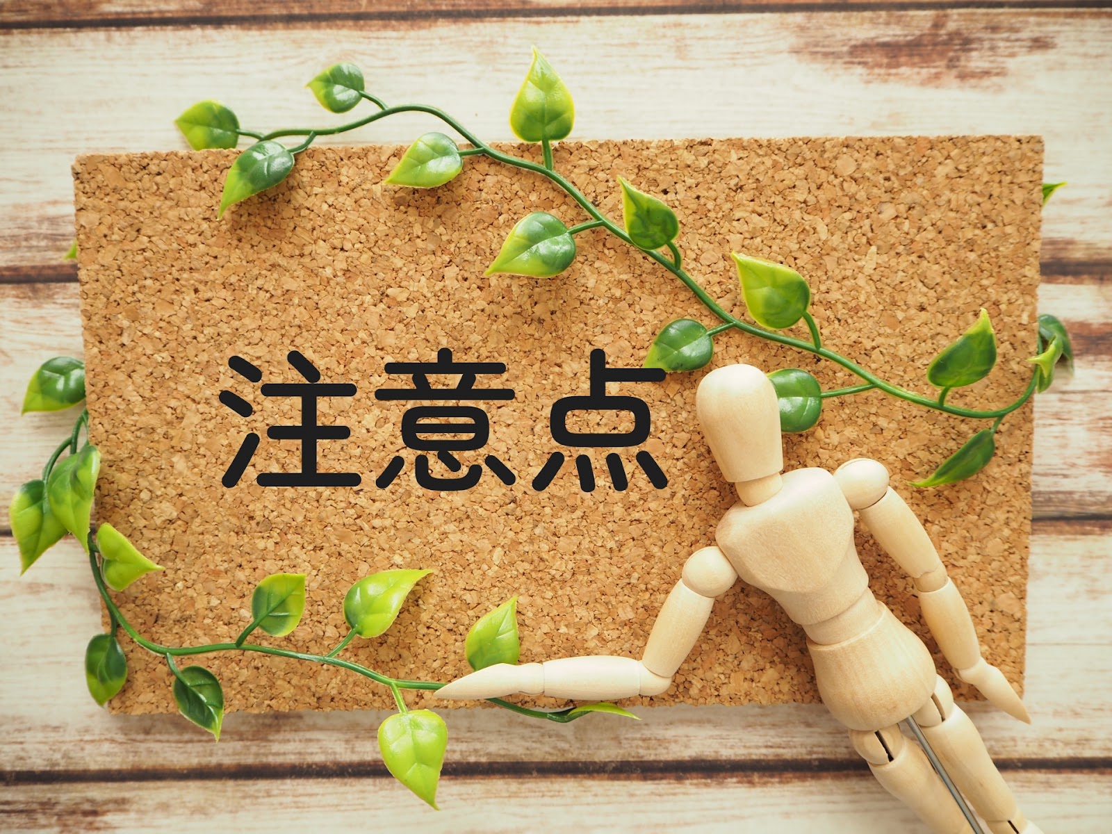 木目の台に置いたコルクボードに「注意点」の文字があり、緑の葉のつると木の人形が添えられた写真