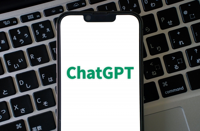ChatGPTの緑のロゴを白い画面に表示したスマホが、パソコンのキーボードの上に置かれた写真