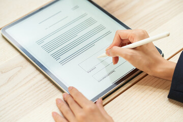 木の机の上に置いたタブレットに表示した書類へ、片手でペンを持って書き込んでいる手元の写真