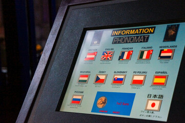 「INFORMATION PHONOMAT」と書かれたパネルに、日本語を含む各国の国旗と言語名が並んだ様子を斜めから写した写真