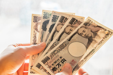 明るい背景の前で、一万円札と五千円札と千円札の紙幣を何枚か扇状に広げて持つ手元の写真