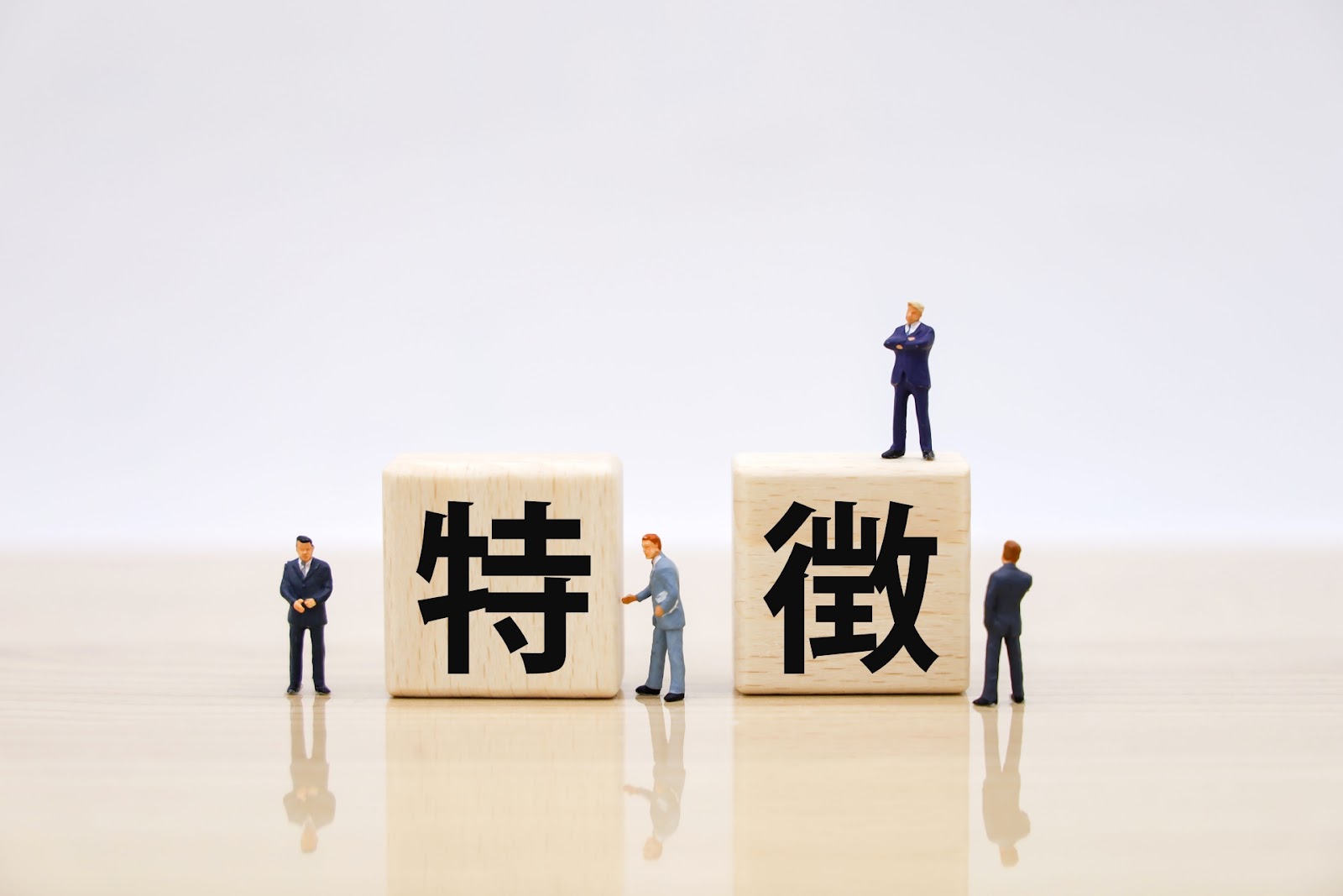 「特徴」の文字が1字ずつ書かれた2つの大きな木のブロックと、その周りに立つスーツ姿の小さな人形が並んだ写真