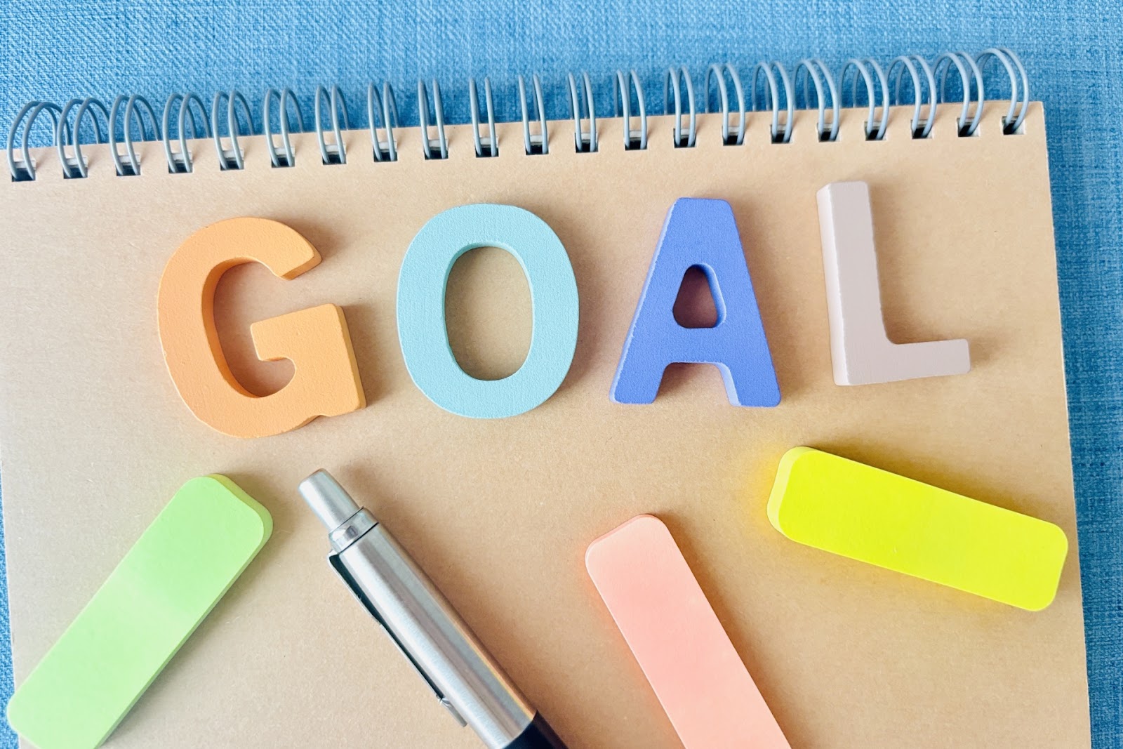 リングノートの上に「GOAL」の立体文字と色違いのふせんとボールペンを並べて真上から撮った写真