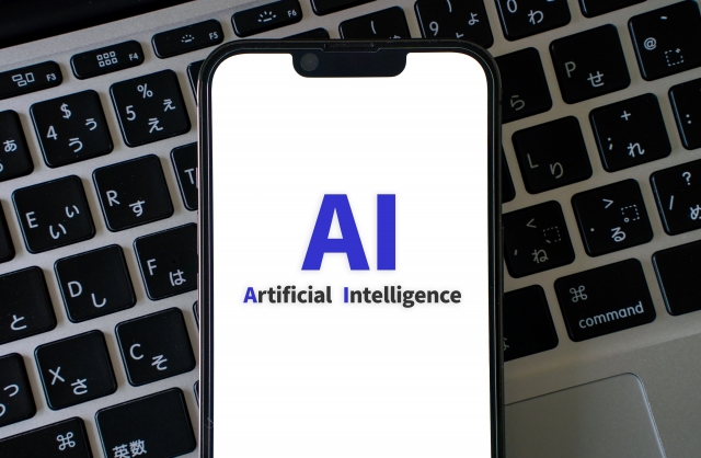 「AI Artificial Intelligence」と表示したスマートフォンをノートパソコンのキーボードに置いた写真