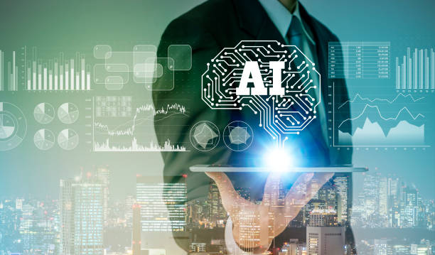 スーツ姿の人物がタブレットを持ち、その上に「AI」と書かれた脳の形の回路やグラフが浮かぶ都市の景色のイメージ画像