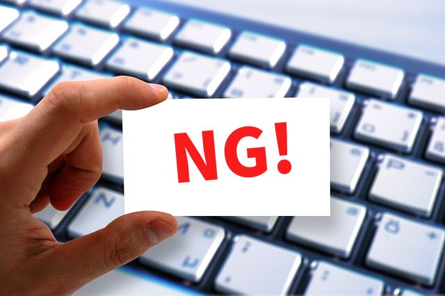 キーボードの手前で、赤い「NG！」の文字が書かれた白いカードを指でつまんで見せている手元の写真