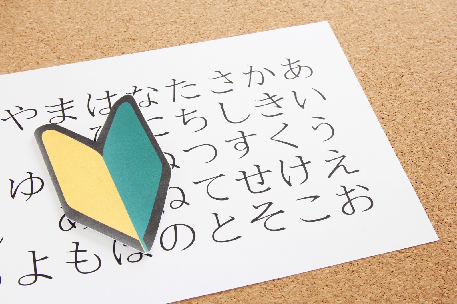 ひらがなの五十音表が大きく書かれた白い紙の上に緑と黄色の初心者マークが置かれた写真