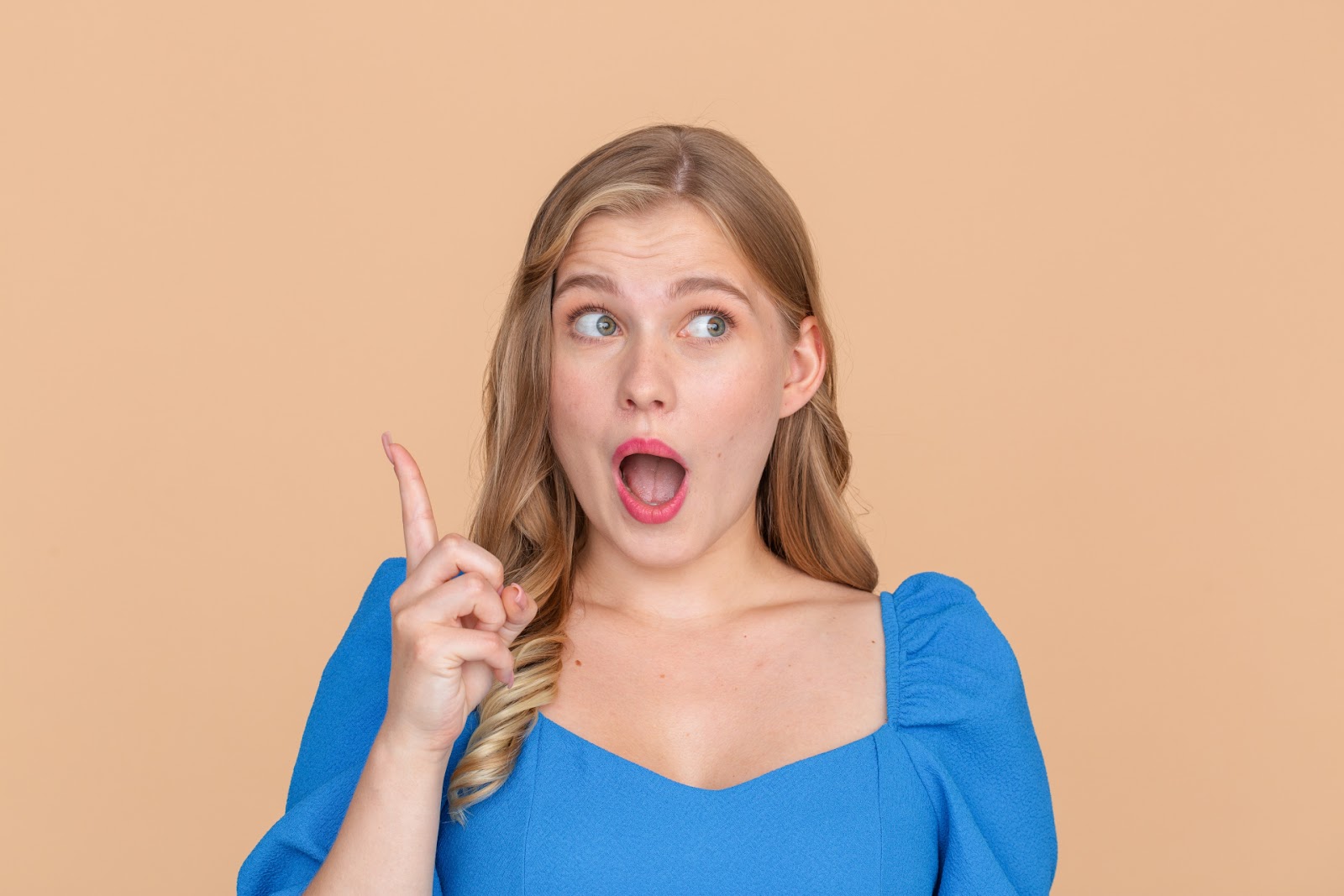 青い服の女性が人差し指を立てて口を開け、ひらめいたような表情をしているオレンジ色の背景の写真