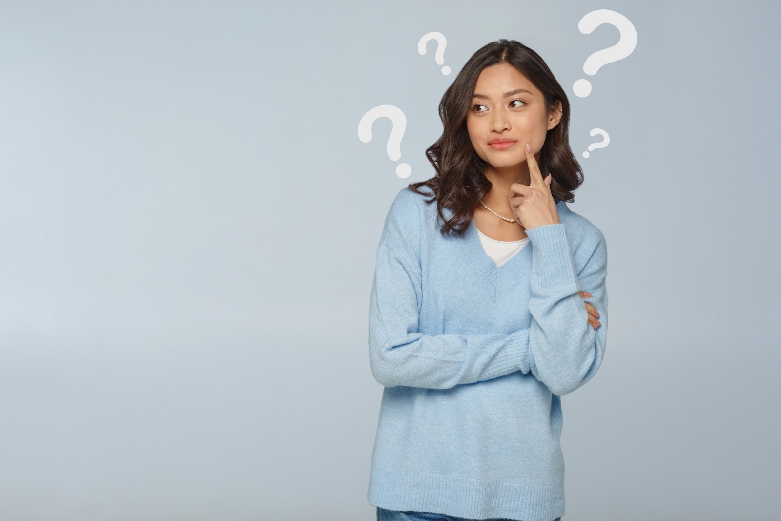 水色のセーターの女性があごに指を当てて横を見ていて、頭のまわりに「？」が浮かんでいる写真